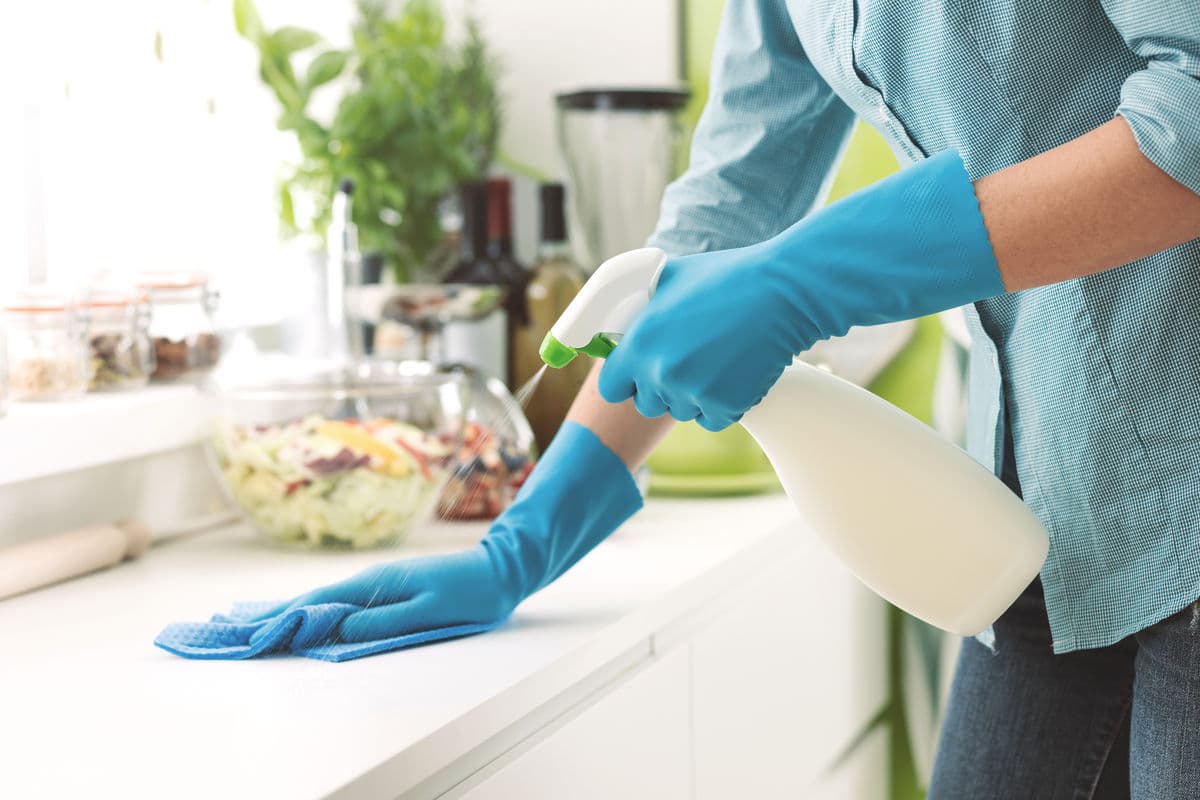 Gloved hand wiping a kitchen counter, room-by-room cleaning tips and checklists.