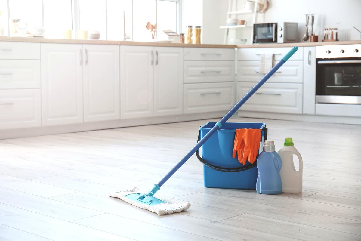 Mop, bucket, gloves, and cleaners in a kitchen, seasonal deep cleaning routine for floors and surfaces.